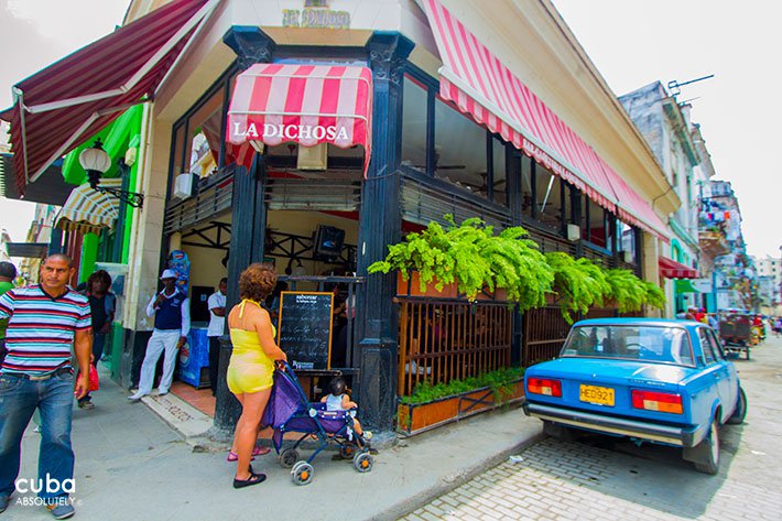 Small bar in Obispo street in Old Havana, people passing by and a blue car park on one side of the bar © Cuba Absolutely, 2014