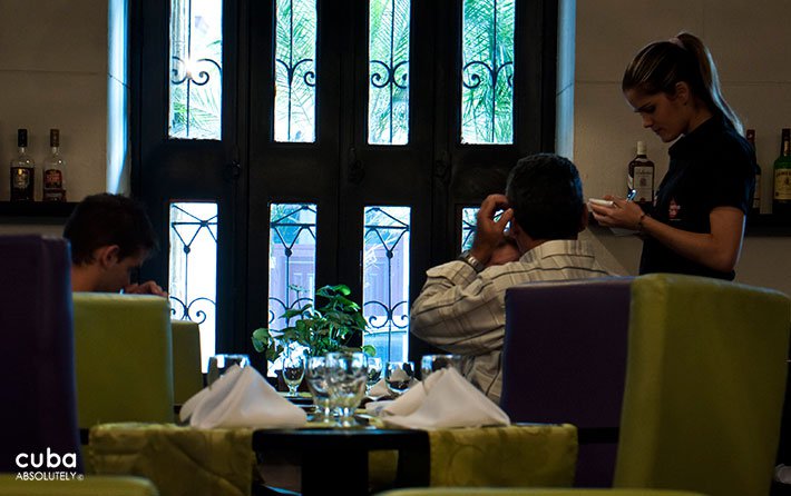 Waiter taking the order to a table at Xana restaurant in Old Havana witn green furnitures © Cuba Absolutely, 2014