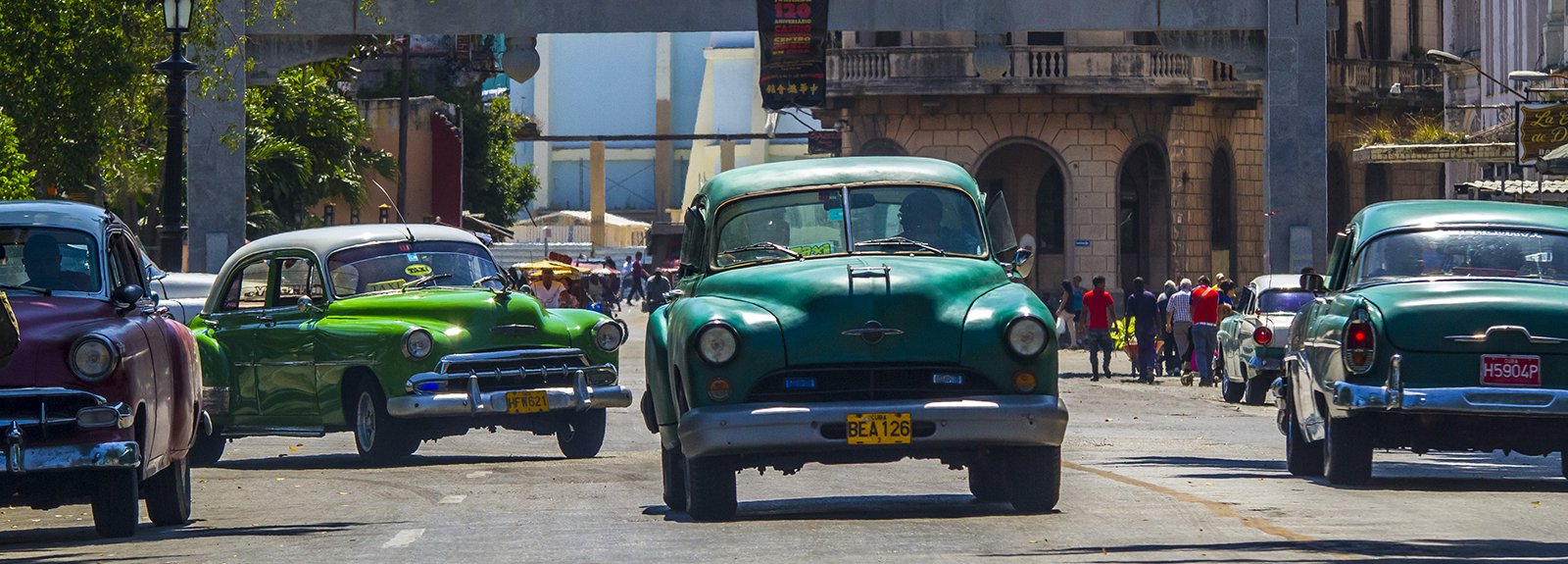 Old cars passing under the entrance of china town , green car in the center