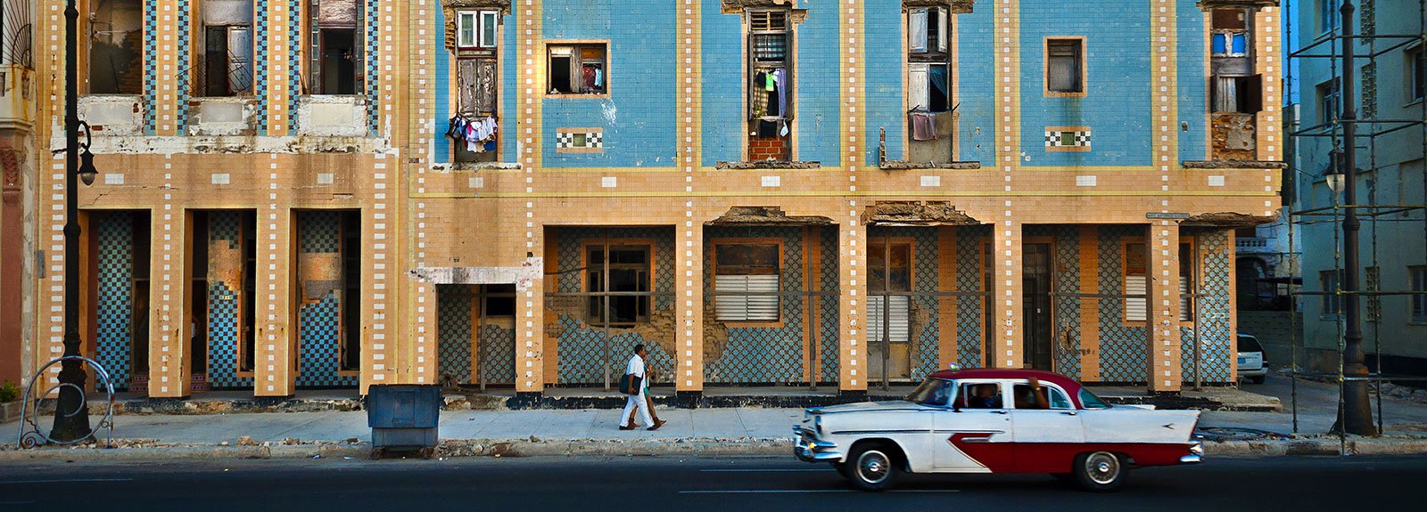 Yellow and blue building with an old car white and red park in front