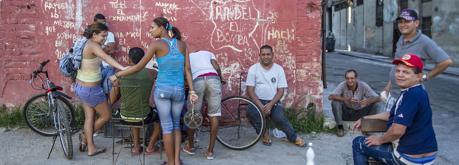 People gattered in a corner against a red wall with chairs and bicycles