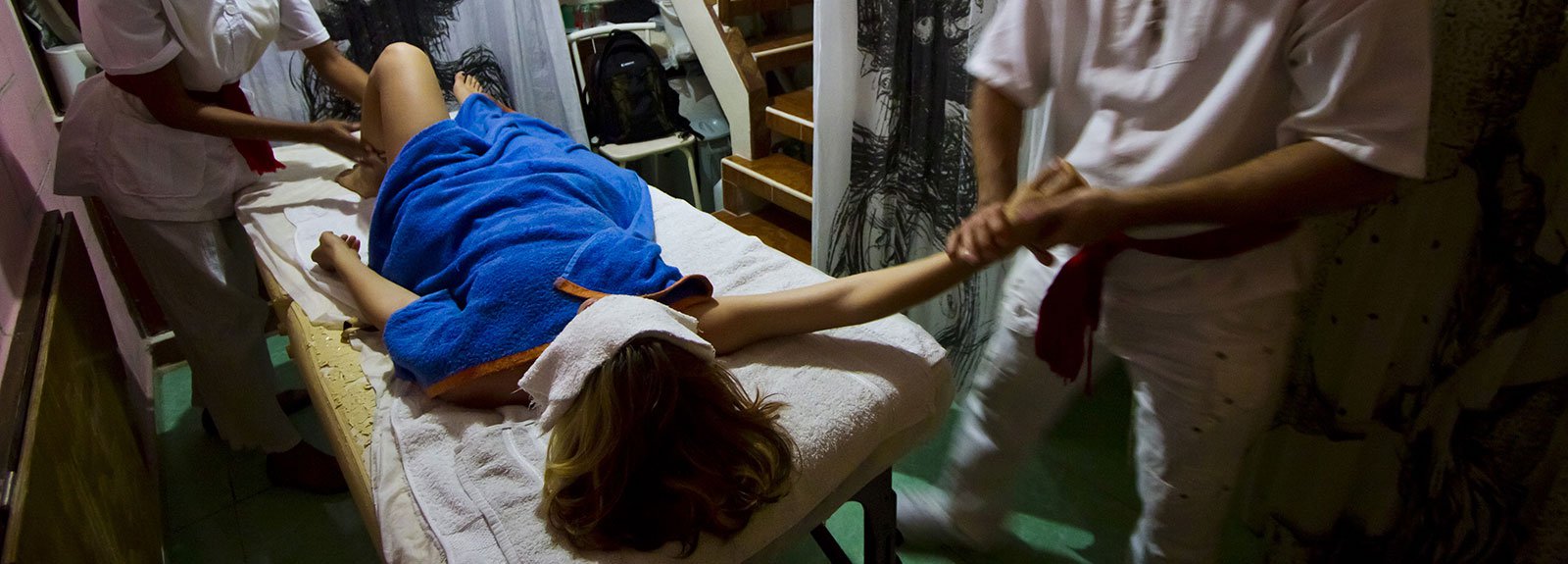 Man and woman dress in white making a massage to a girl cover with a blue towell