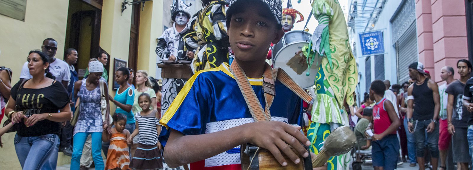 Kid playing a drum with a big colorfull parade behind him