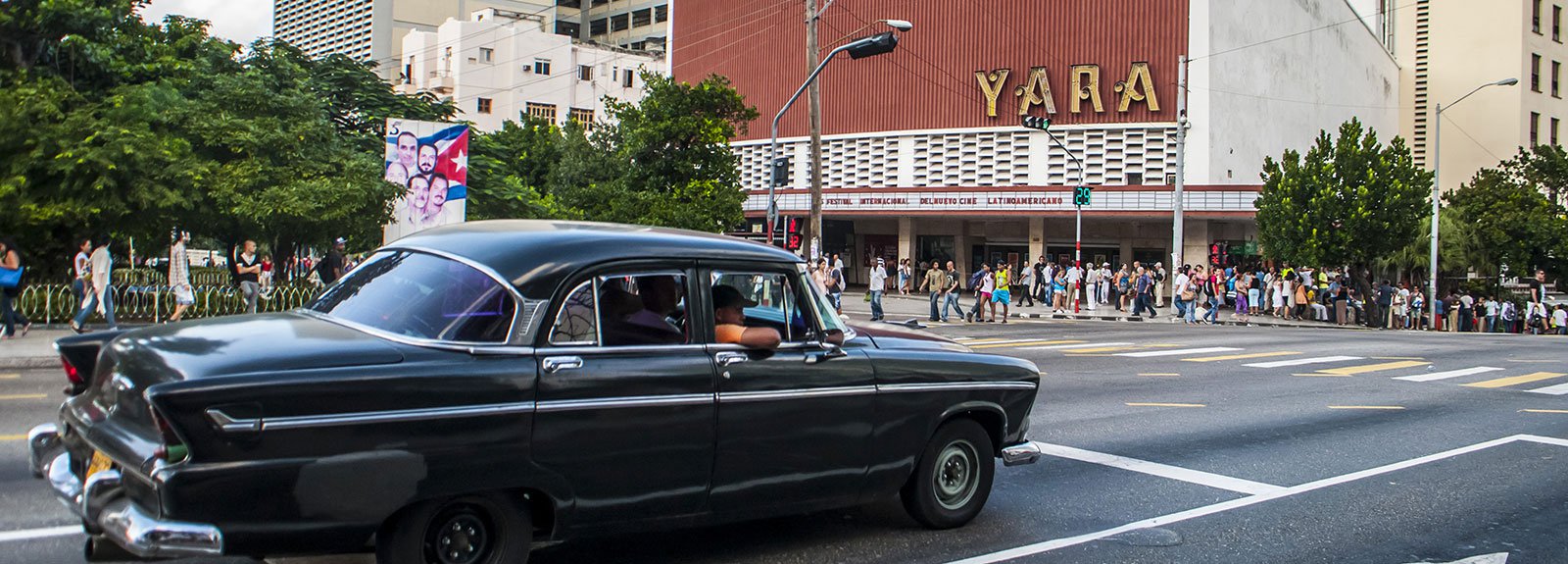 Old green car passing across Yara cinema